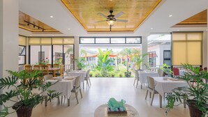 Amplio espacio interior con mesas y sillas, un ventilador de techo y grandes ventanales que ofrecen vistas al exterior.