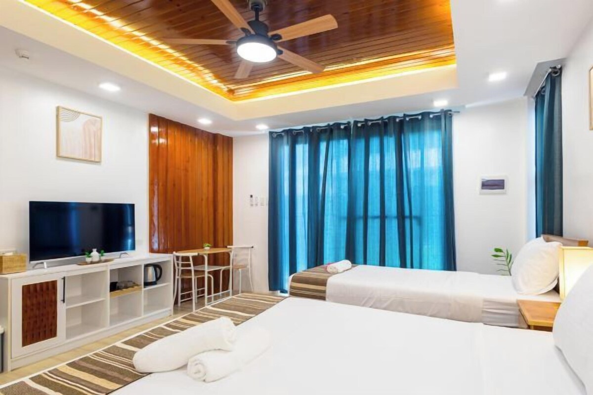 Ein Hotelzimmer mit zwei Betten, einem Fernseher, einem Schreibtisch und einem Deckenventilator.