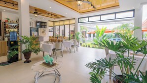 Amplio espacio interior con mesas y sillas, ventilador de techo y grandes ventanales que ofrecen vistas al exterior.