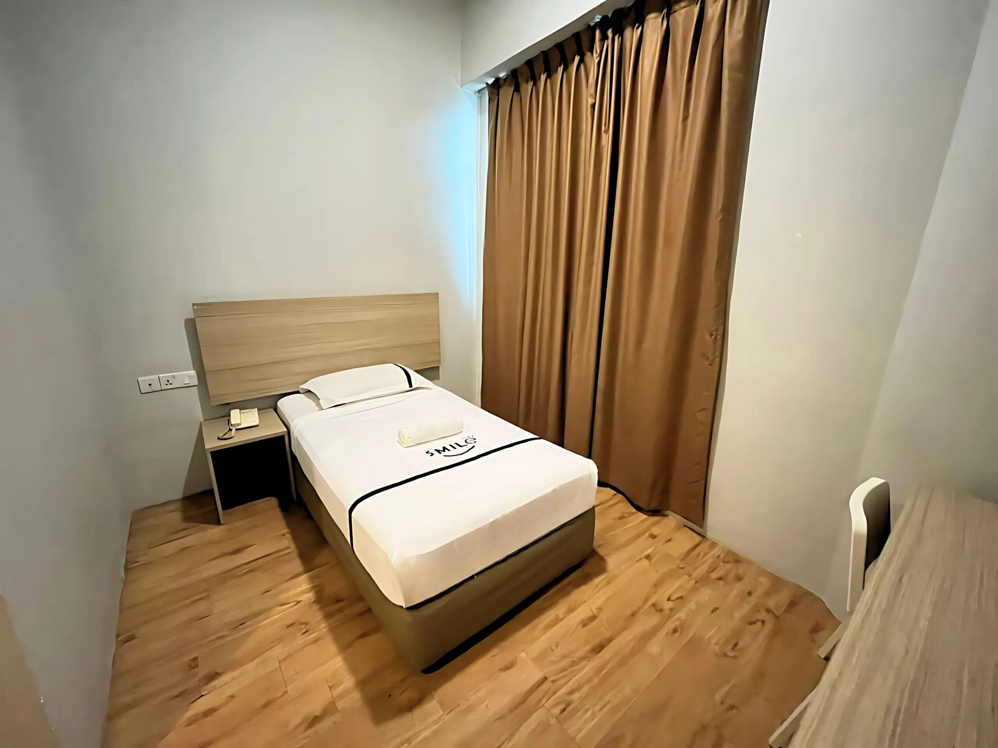 Une chambre d’hôtel avec un lit en bois, une table de chevet avec un téléphone et un rideau.
