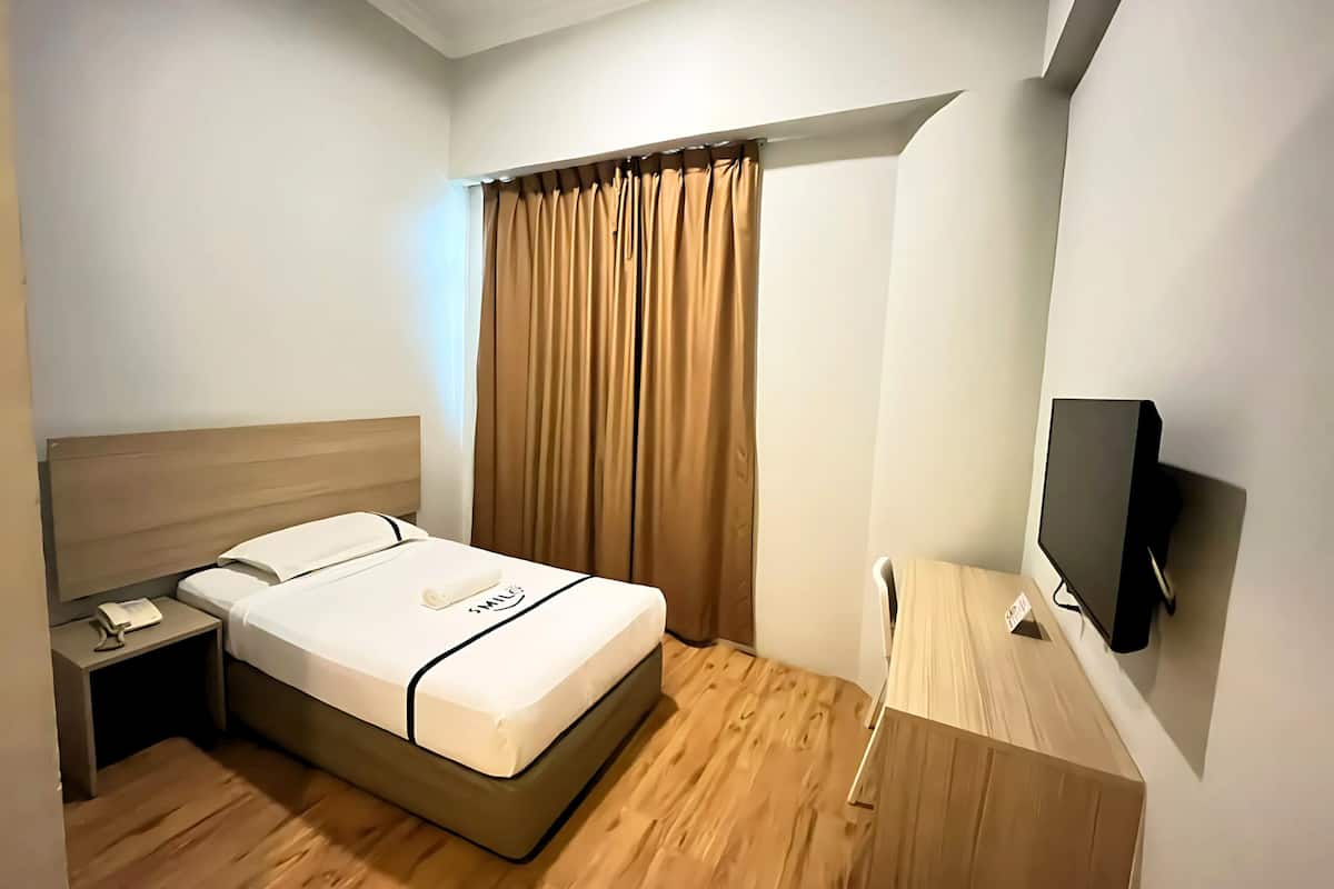 Een hotelkamer met een bed, een nachtkastje met telefoon, een aan de muur bevestigde televisie en een raam met gordijnen.