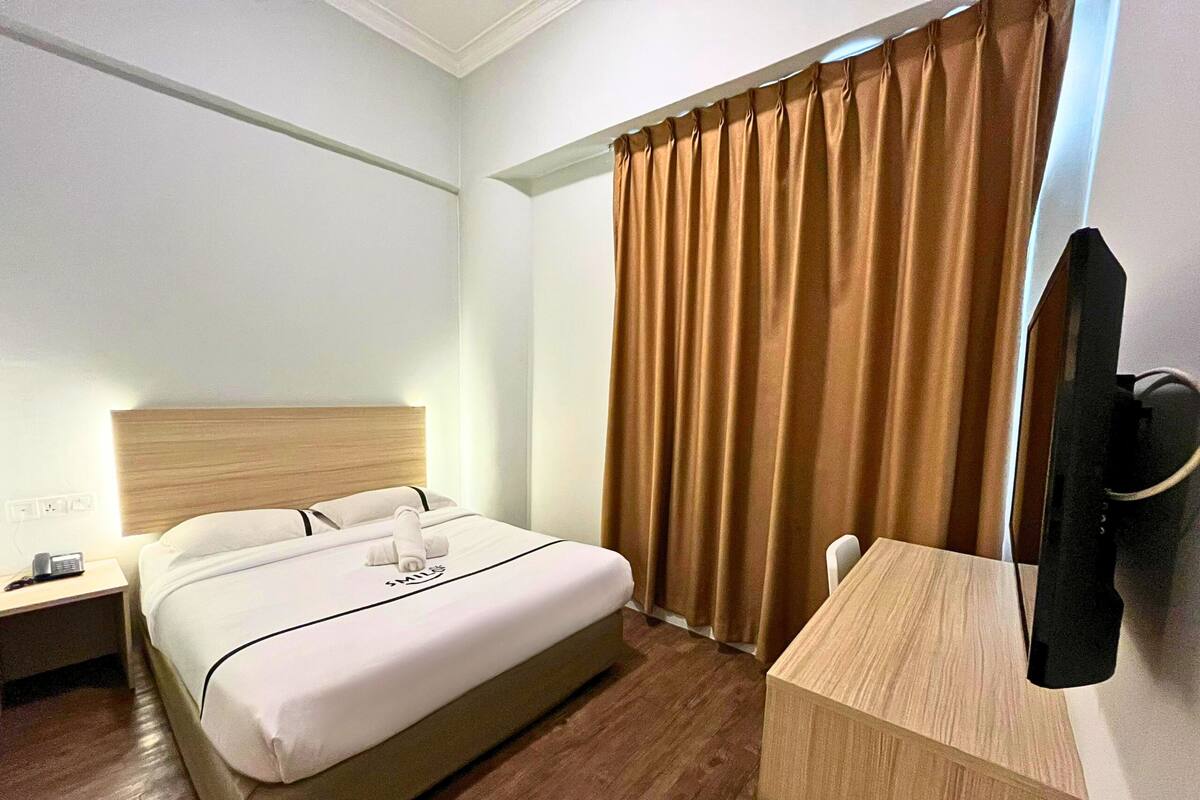Een hotelkamer met een bed, bureau, stoel, televisie en gordijn.