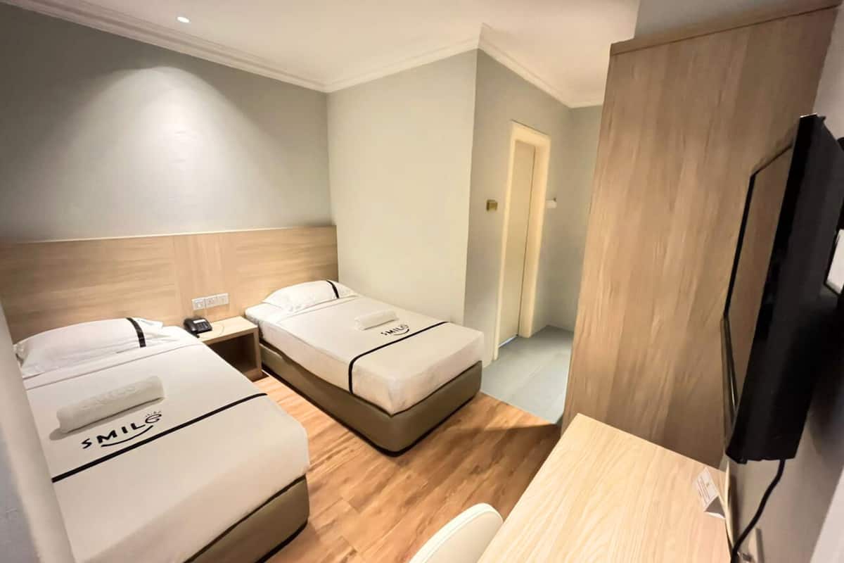Een hotelkamer met twee bedden, een bureau, een stoel, een televisie en een houten garderobe.