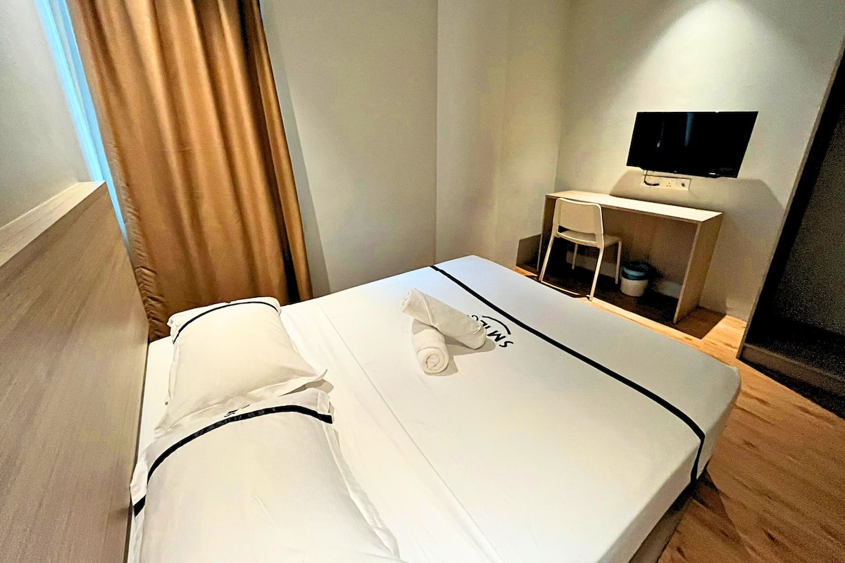 Een hotelkamer met een bed, een televisie op een standaard en een kleine tafel met een stoel.