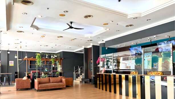 A modern hotel lobby with a wooden floor, a brown sofa, a ceiling fan, and a reception desk with a TV. - Sky Hotel Chow Kit PWTC (Kuala Lumpur)