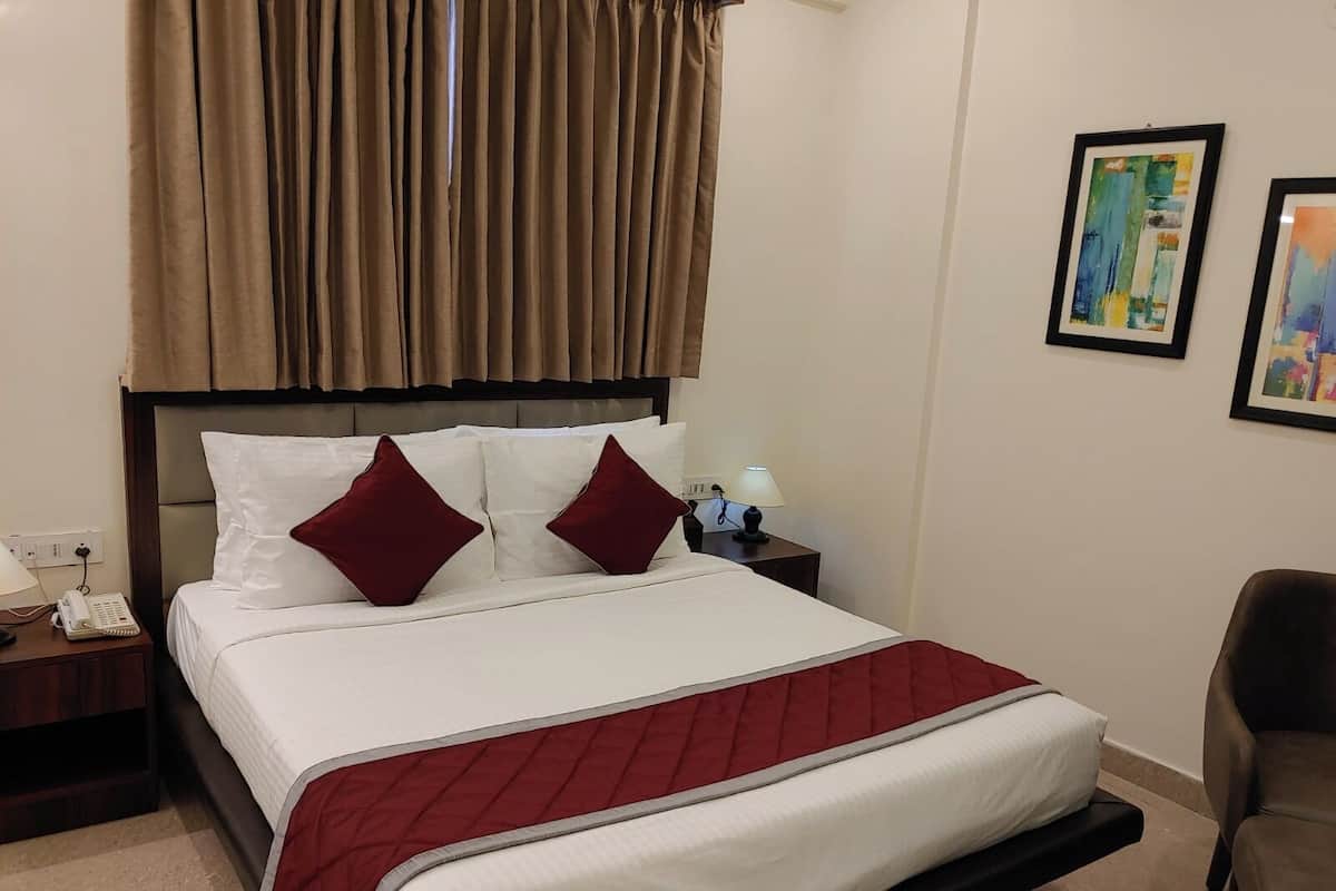 Een hotelkamer met een bed, een nachtkastje met een lamp, een stoel en twee ingelijste kunstwerken aan de muur.