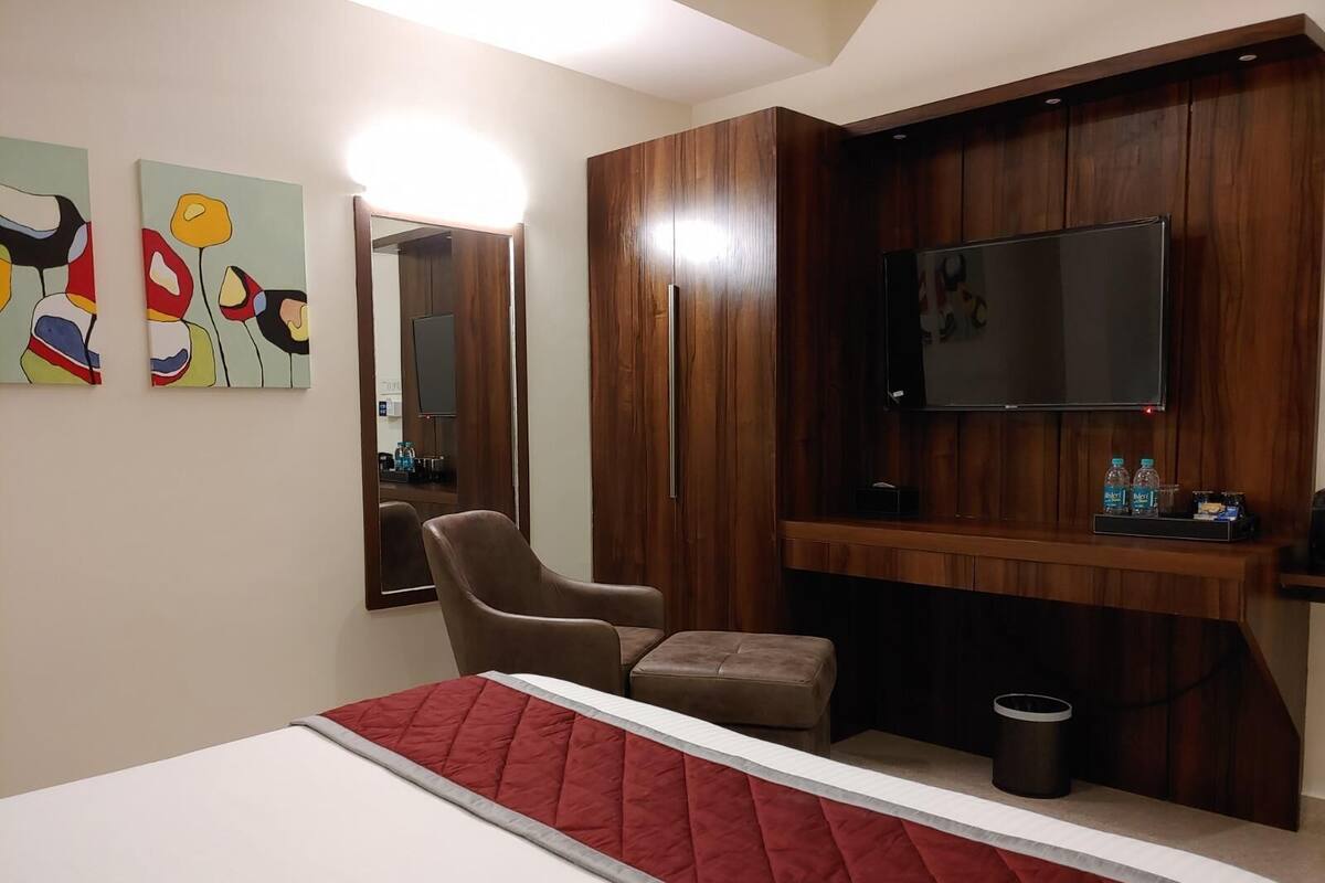 Een hotelkamer met een bed, een stoel, een televisie en een spiegel.
