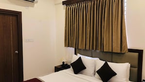 Habitación de hotel con cama, mesita de noche, lámpara, teléfono y ventana con cortinas.