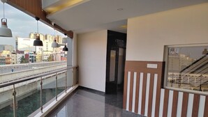 Un corredor moderno de hotel con barandilla de cristal que da a un puente y vistas de la ciudad, suelo pulido y una escalera con pared a rayas.