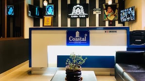 Una mesa de recepción con un cartel de Coastal Grand Hotels & Resorts, un letrero de no fumar y un televisor que muestra varios canales.