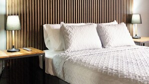 Een moderne slaapkamer met een houten lattenbovenstuk, een groot bed met witte beddengoed, twee nachtkastjes met lampen, en een klein nachtkastje.