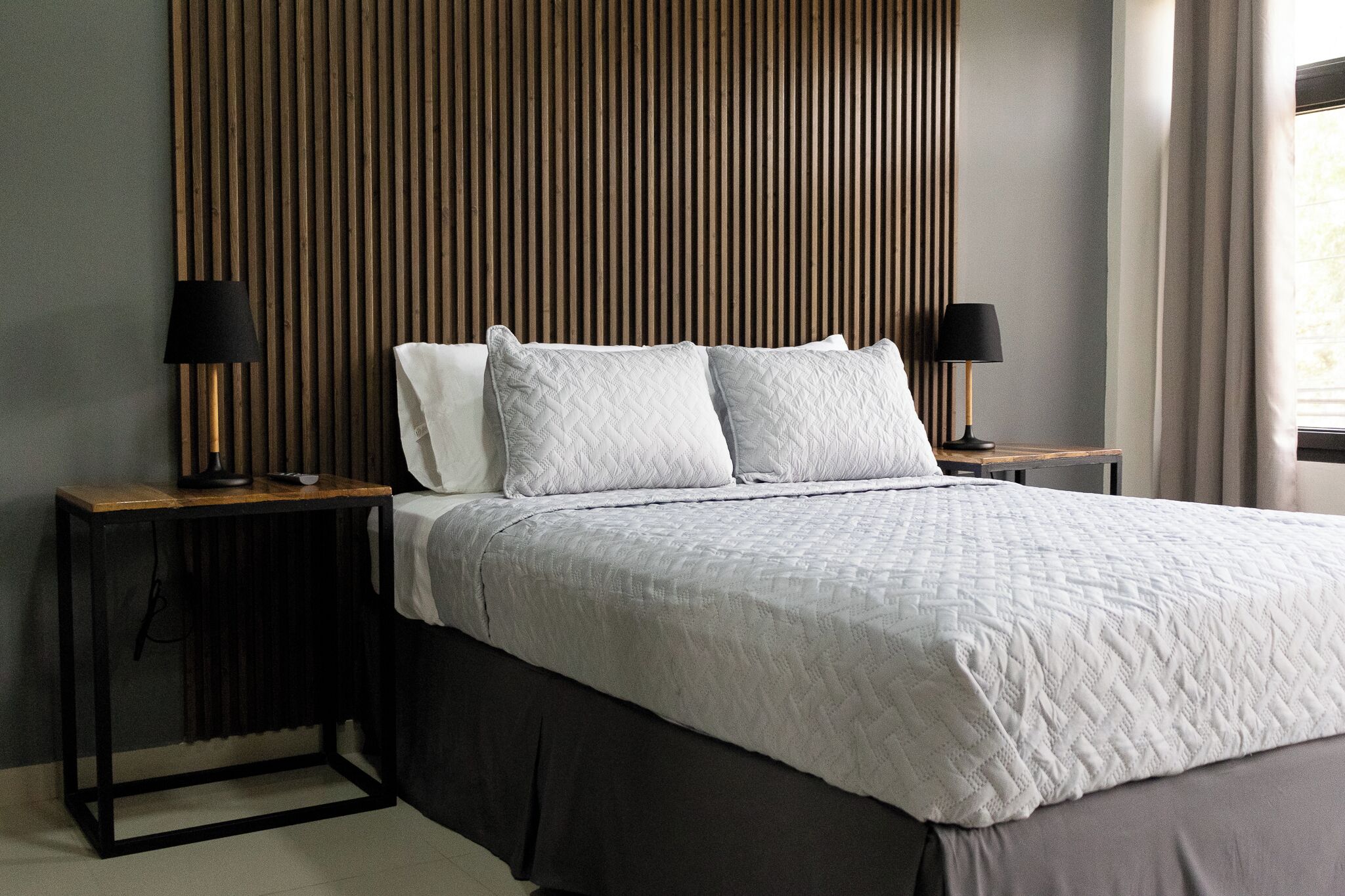 Un dormitorio moderno con una cama grande, dos mesitas de noche y un cabecero de listones de madera.