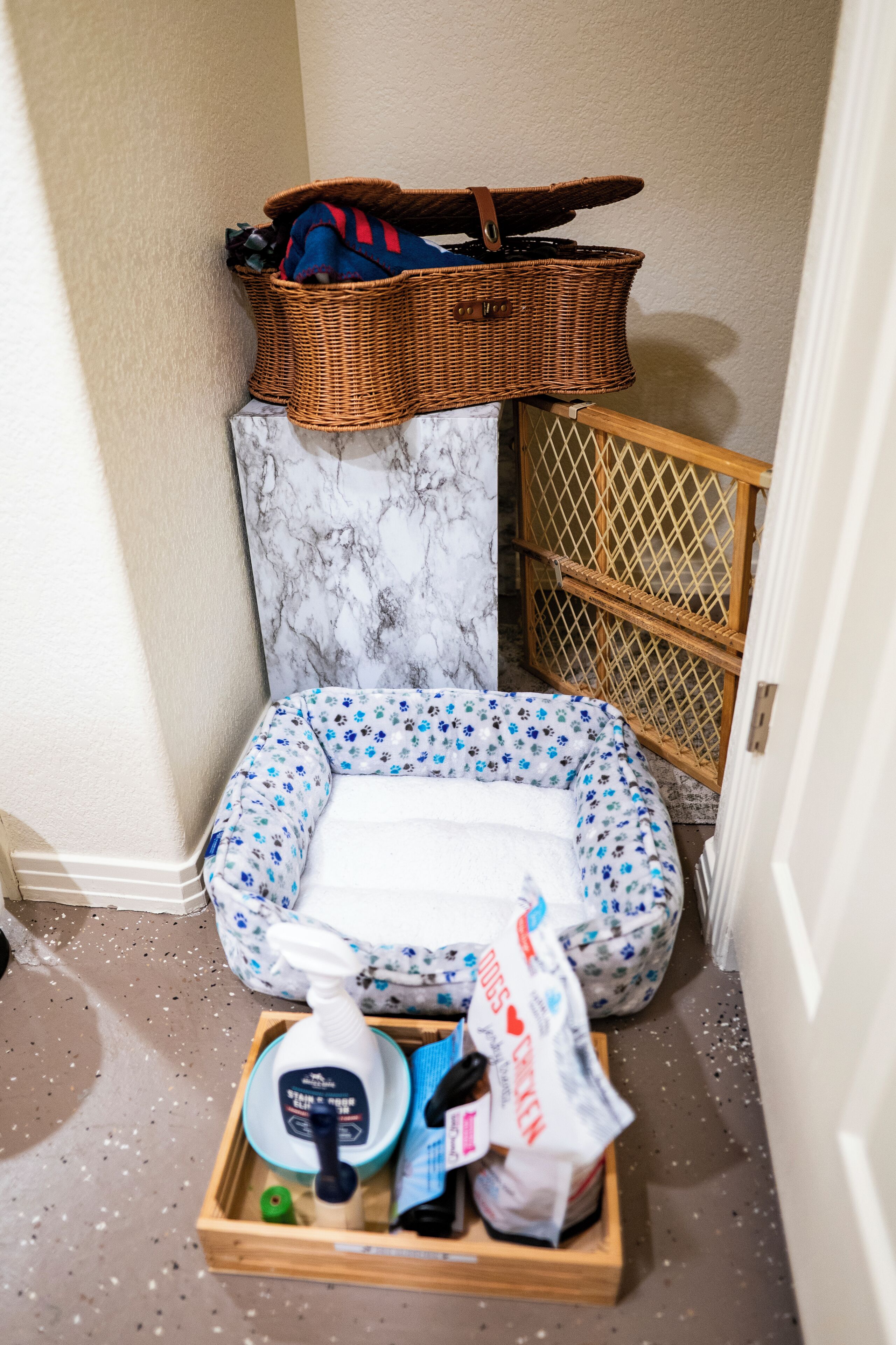 A corner of a room with a wicker basket, a baby bathtub, and a wooden crate with cleaning supplies.
