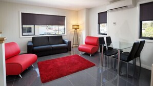 A modern living room with a black sofa, red chairs, and a glass dining table.