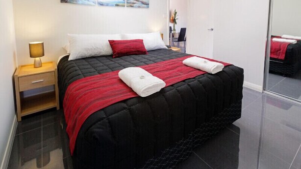 A modern bedroom with a black quilted bedspread, white and red pillows, a bedside lamp, and a painting of a waterfall on the wall.