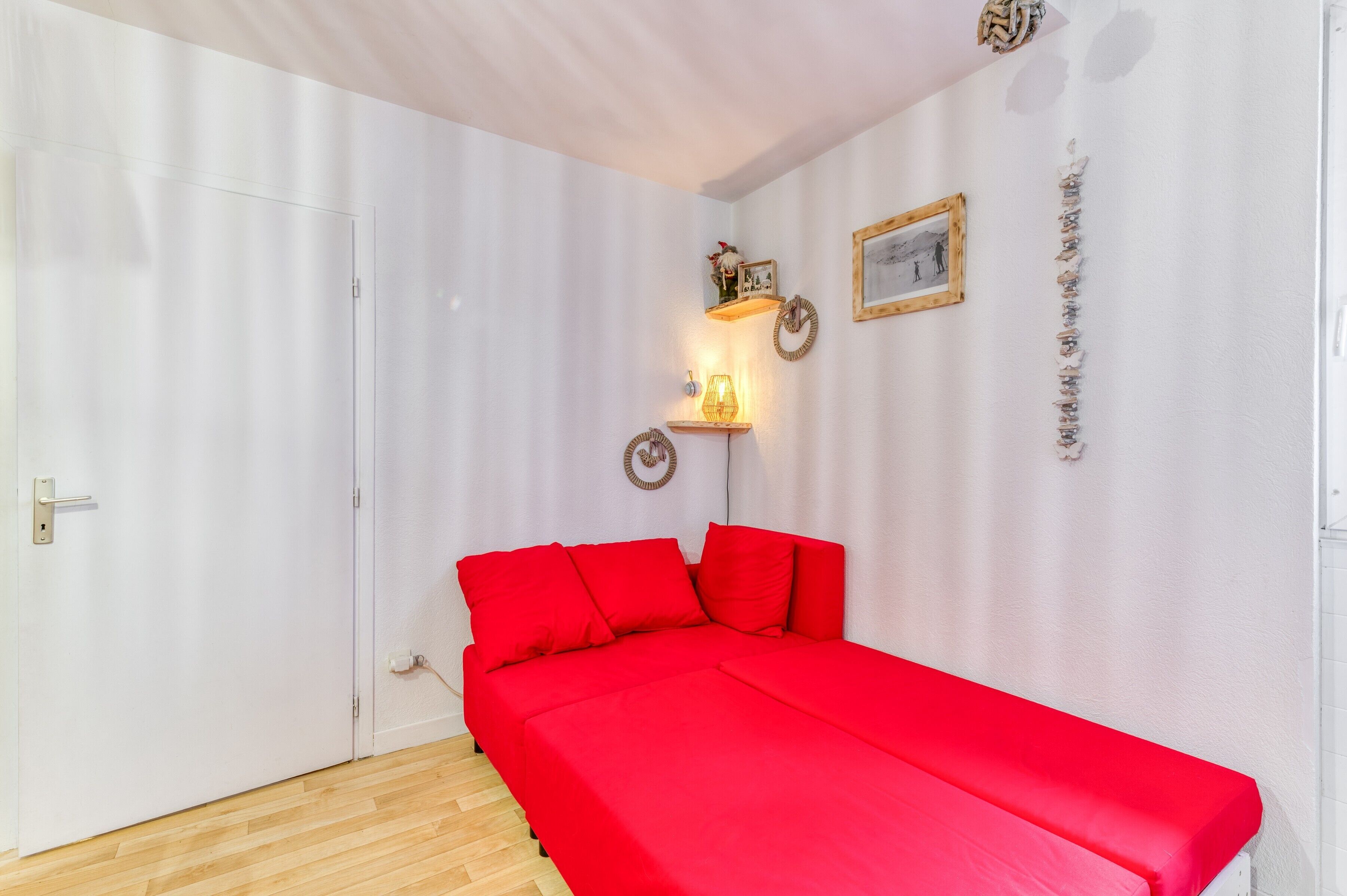 Une pièce comprenant un lit, une porte, une étagère fixée au mur avec une lampe, et un tableau encadré.