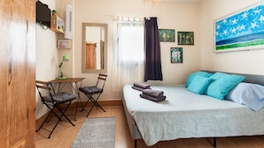 Un dormitorio con una cama, un escritorio, sillas, una lámpara colgante y un cuadro en la pared.