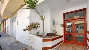 Entrada de un edificio con puerta roja, una jardinera pequeña con plantas y pavimento de baldosas.