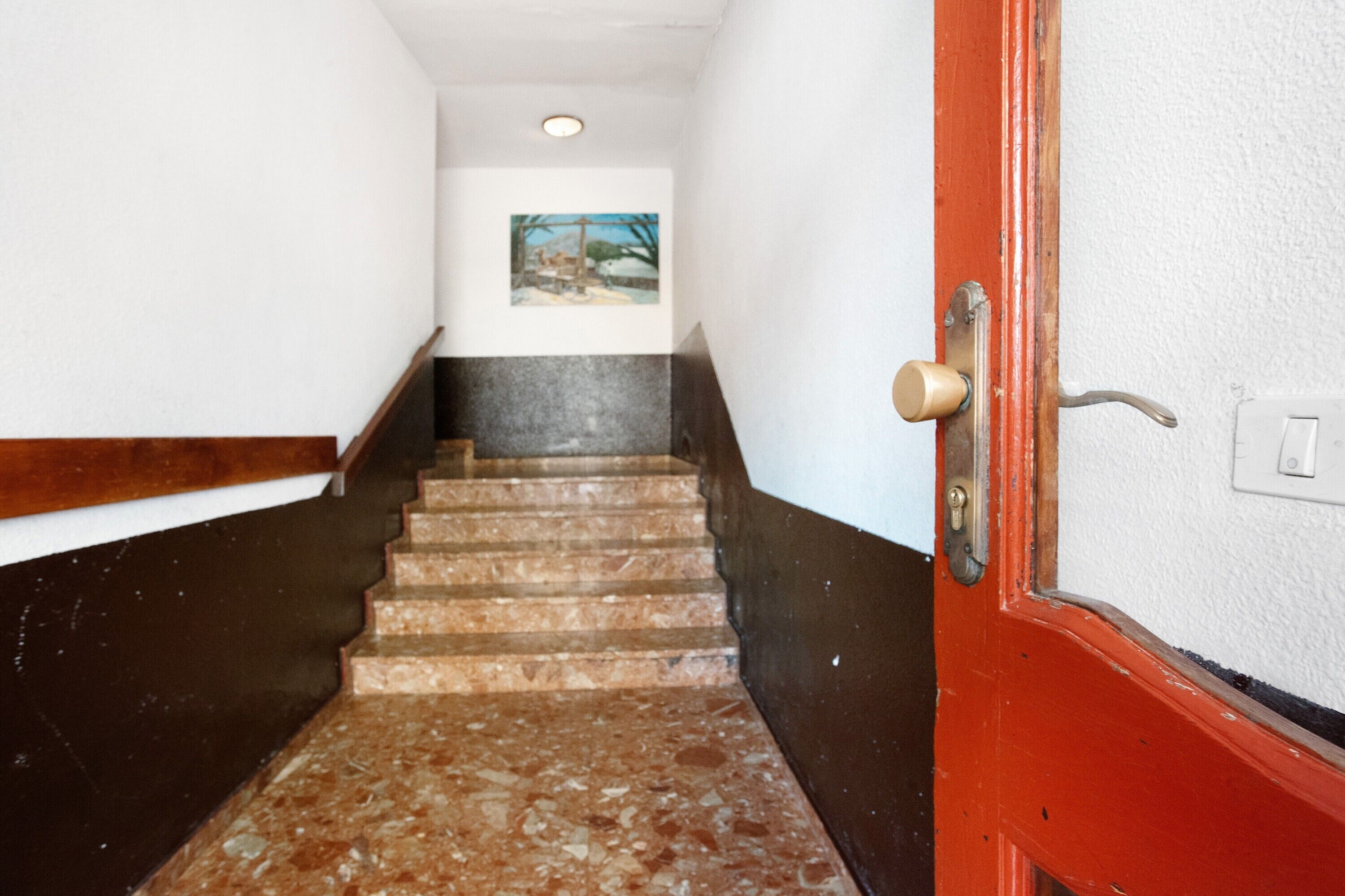 Una escalera con barandilla, una puerta con manija de latón y una lámpara de pared.