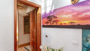 Un pasillo con una puerta de madera, un espejo, una lámpara de pared y un cuadro de un atardecer.