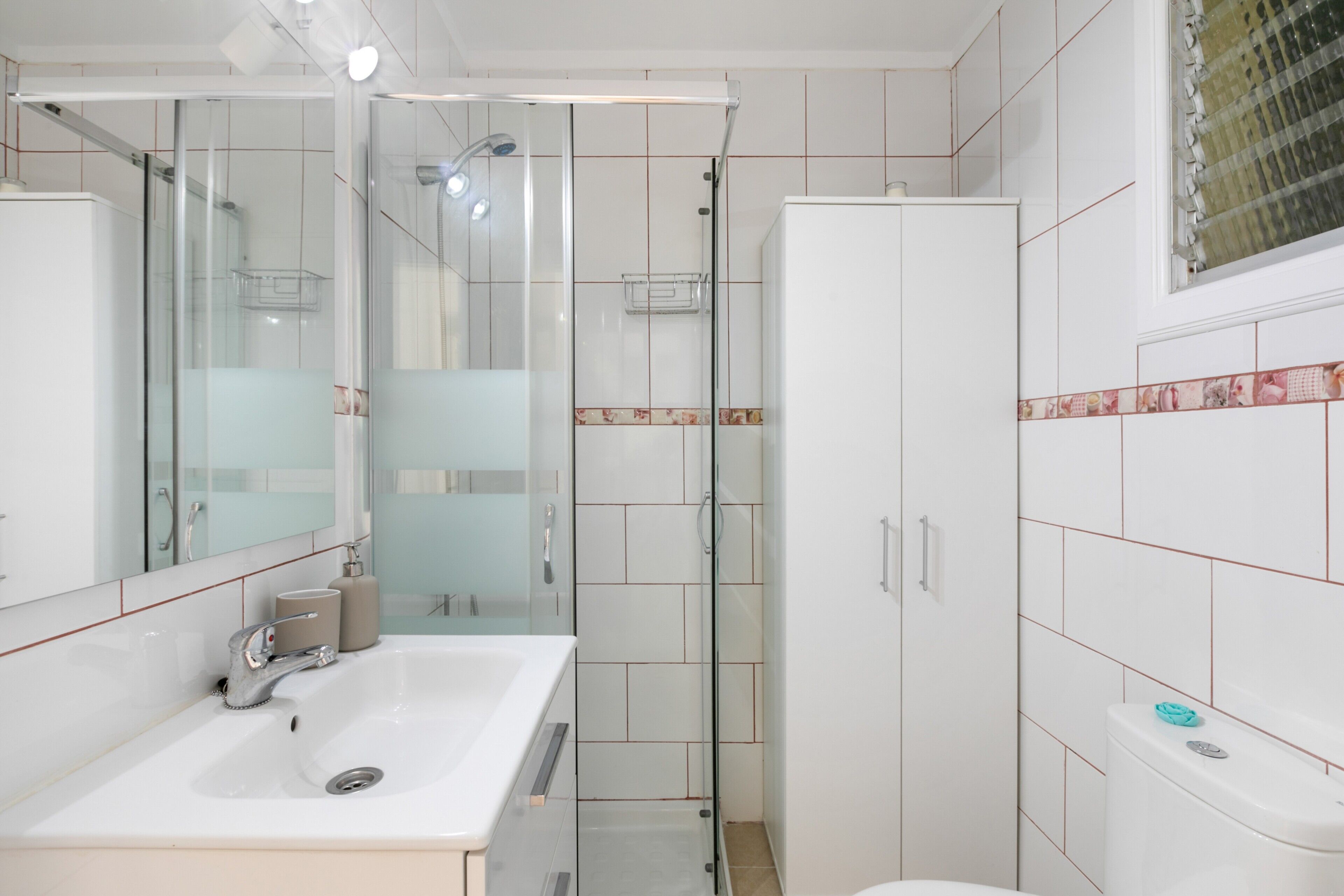 Un baño con lavabo, espejo, ducha, inodoro y armarios.
