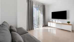 Una sala de estar moderna con un sofá, un televisor montado en la pared, una mesa consola de madera y un gran ventanal corredizo.
