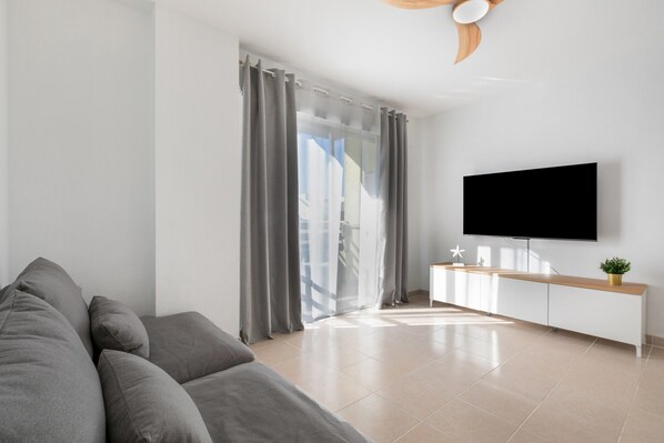 Una sala de estar moderna con un sofá, un televisor montado en la pared, una mesa consola de madera y un gran ventanal corredizo.