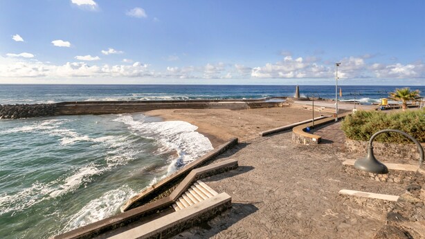 Un paseo marítimo con barandilla de piedra, escaleras que bajan a la playa y un farol.