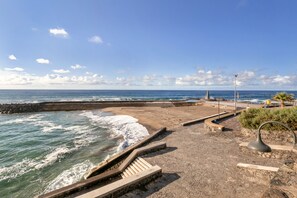 Un paseo marítimo con barandilla de piedra, escaleras que bajan a la playa y un farol.