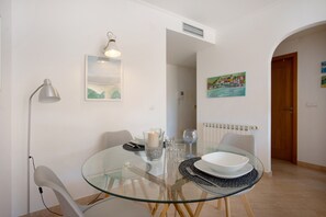 A dining area with a glass table, white chairs, a candle, and a painting on the wall.