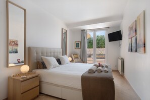 A bedroom with a bed, bedside table, lamp, and a view of the outdoors.