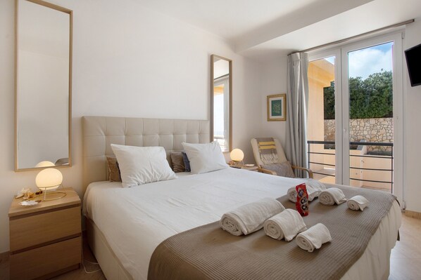 A hotel room with a large bed, a bedside table with a lamp, a chair, and a view of the outdoors through a sliding door.