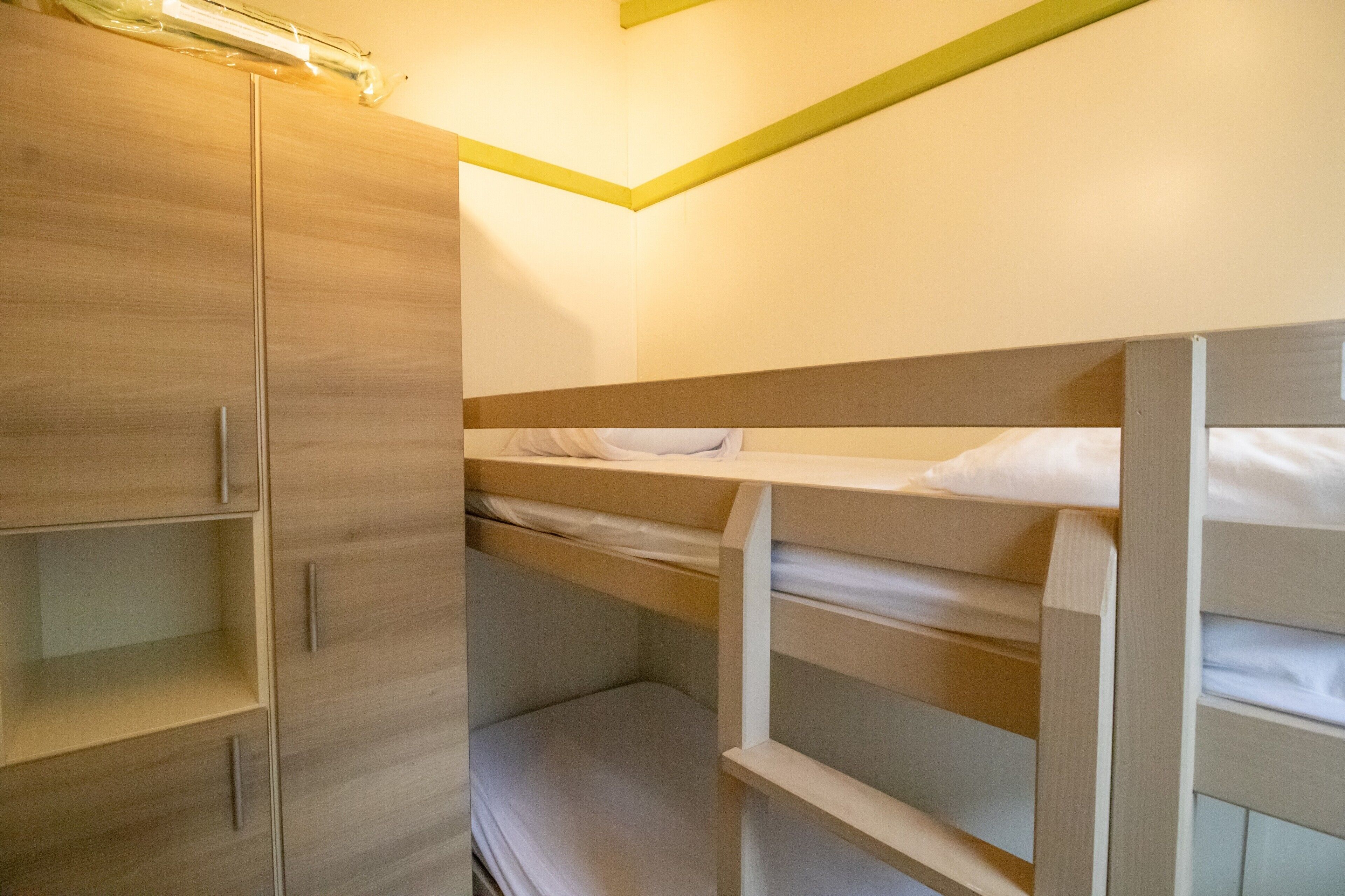 En køjeseng med træsengestykke, en garderobe med spejl og en lysarmatur i loftet.