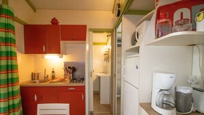 A compact kitchen with a red cabinet, a white table, and a coffee maker. - Mobile Home 'Chalet Confort Proche De La Mer' with Shared Pool, Private Terrace and Air Conditioning (Pianottoli-Caldarello)