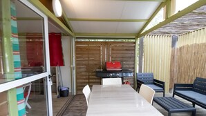 An outdoor patio with a table and chairs, a grill, and a covered area. - Mobile Home 'Chalet Confort Proche De La Mer' with Shared Pool, Private Terrace and Air Conditioning (Pianottoli-Caldarello)