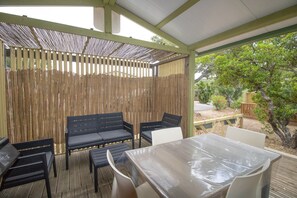 Un espace extérieur abrité, avec une table et des chaises, une clôture en bambou et une vue sur le jardin.