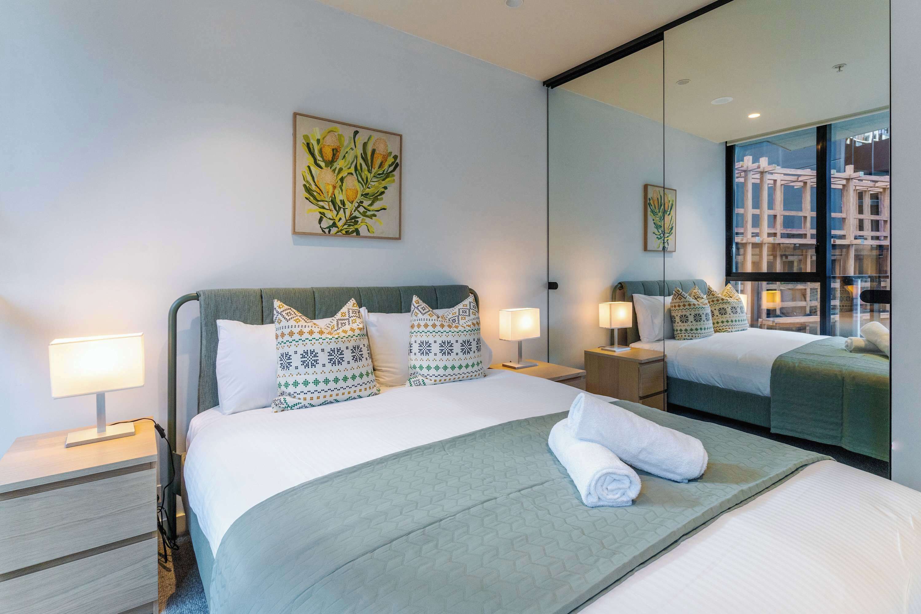 Habitación de hotel con una cama grande, dos mesitas de noche, un espejo y una ventana con vistas a la ciudad.