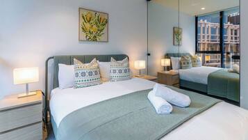 Habitación de hotel con una cama grande, dos mesitas de noche, un espejo y una ventana con vistas a la ciudad.