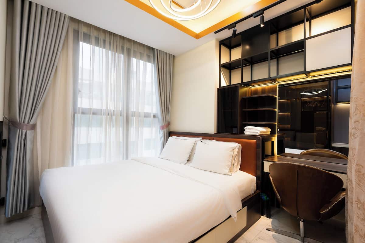 A modern hotel room with a large bed, a desk, and a built-in wardrobe.