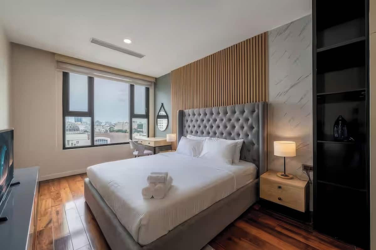 A hotel room with a large bed, a desk, a chair, a TV, a window with a city view, and a wardrobe.