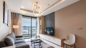 A modern living room with a sofa, a TV, a chair, and a small table. - Salute de Madison Luxury Apt District 1 (Ho Chi Minh City)