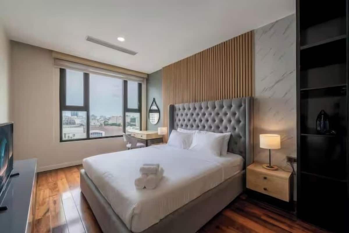 A hotel room with a large bed, a TV, a desk, and a view of the city through the window.