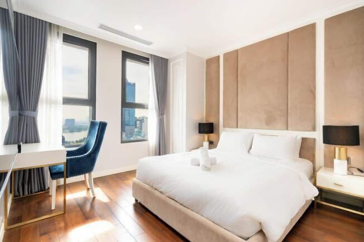 A hotel room with a bed, a desk, a chair, a nightstand, and a view of the city.