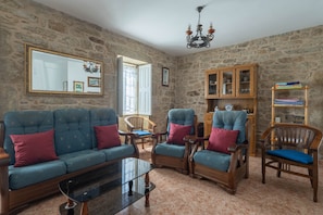 A stone-walled room with a sofa, armchairs, a wooden cabinet, and a glass coffee table.