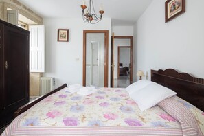 A bedroom with a bed, a wardrobe, a chandelier, and a door leading to another room.