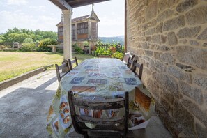 A covered outdoor dining area with a table set for four, stone walls, and a view of a traditional building in the background.