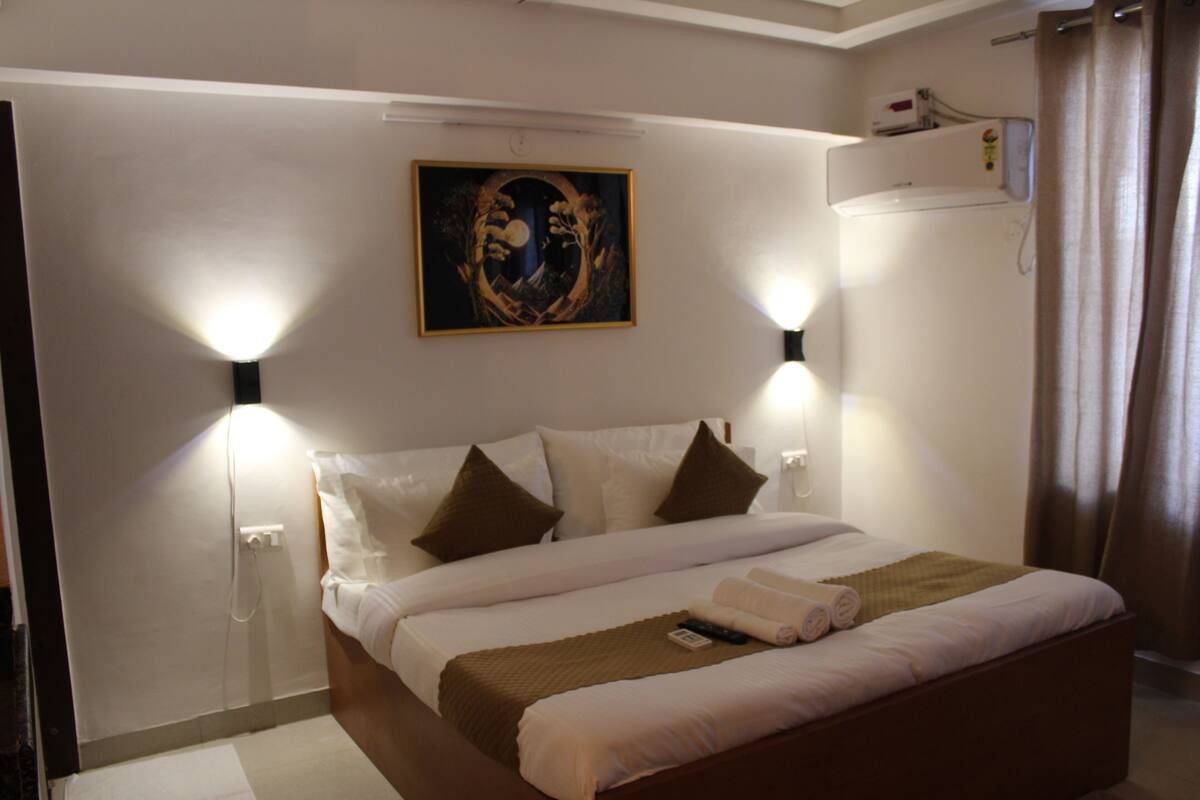 A neatly made bed with a blanket, pillows, and a remote control. There are two wall-mounted lights and a painting above the bed.