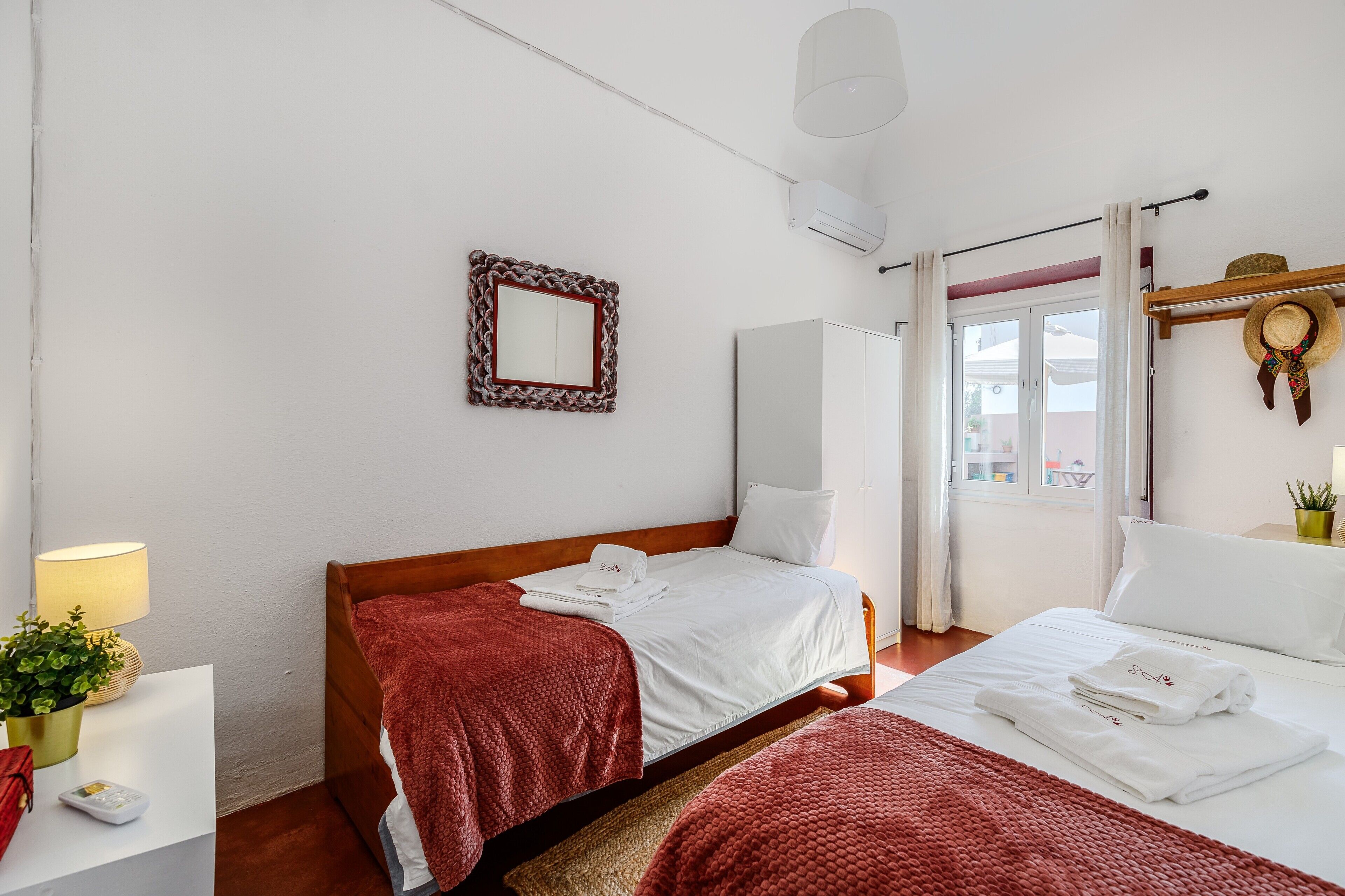 Habitación de hotel con dos camas, una mesita de noche con lámpara, un espejo y una ventana con cortinas.