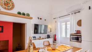 A modern kitchen with a flat-screen TV, microwave, and a small dining area with a wooden table and chairs.