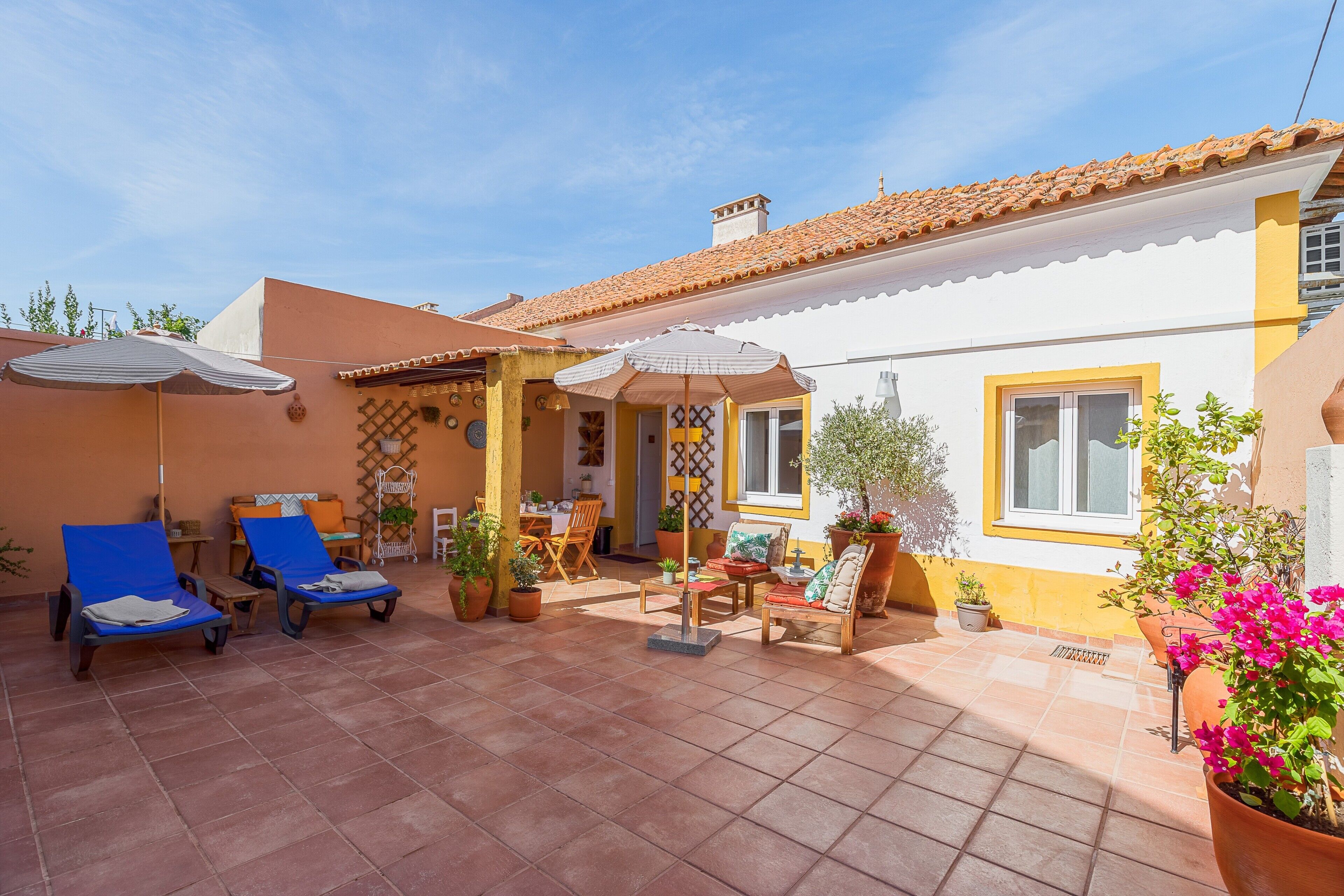 Une terrasse avec des chaises longues, une table, des chaises et des plantes en pot.